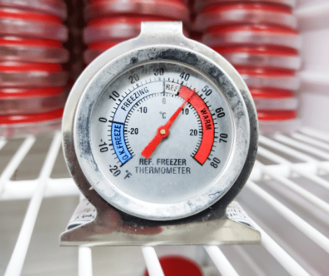 Refrigerator thermometer sitting on the shelf with food storage containers in the background. The thermometer indicting unsafe temperatures.