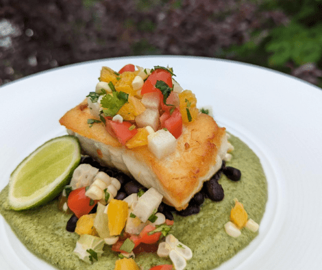 Piece of seared group topped with corn salsa plated in a bowl or broccoli based mole.