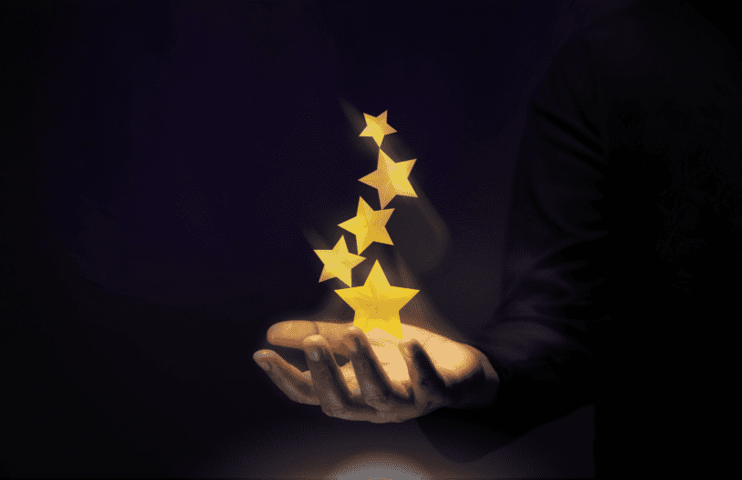 abstract image of five gold stars floating up and out of an outreached hand against a completely dark/black background.